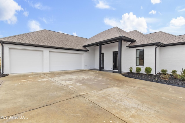 view of front facade featuring a garage, concrete driveway, roof with shingles, and brick siding