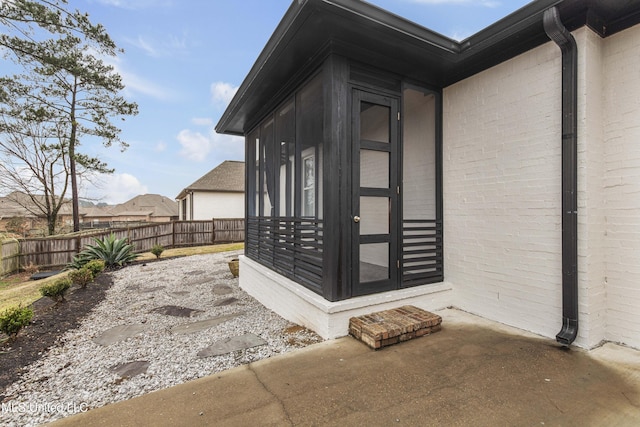 entrance to property featuring a patio area, fence, and brick siding