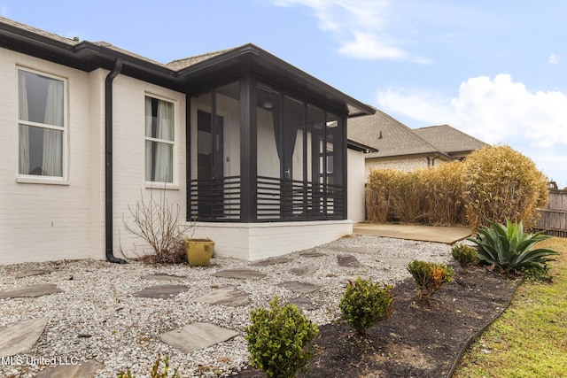 view of property exterior with a sunroom, fence, and brick siding