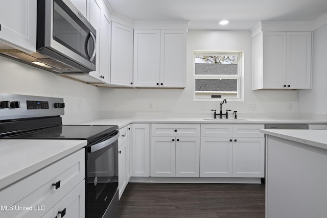 kitchen with a sink, light countertops, white cabinets, dark wood-type flooring, and appliances with stainless steel finishes