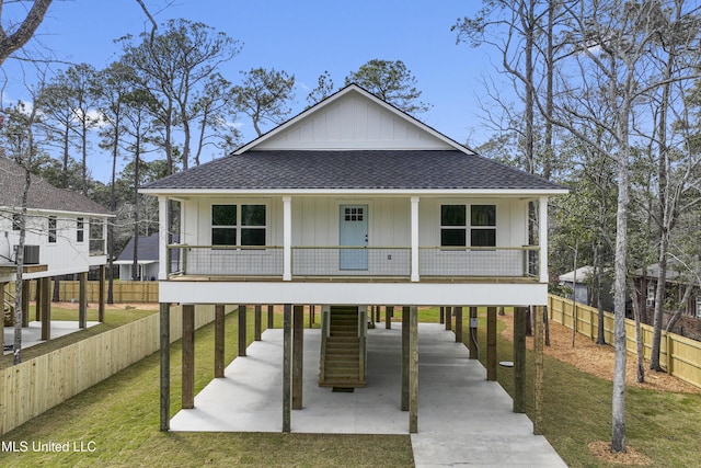 beach home featuring a porch, roof with shingles, concrete driveway, a carport, and stairs