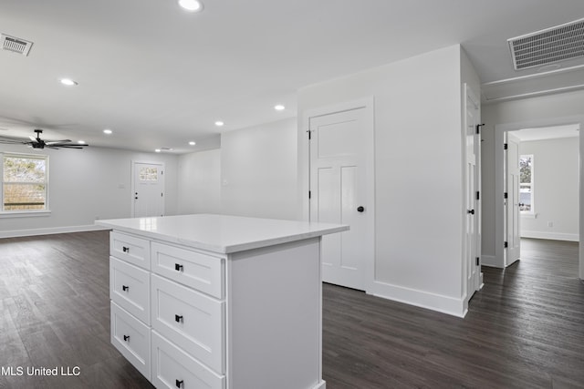 interior space featuring white cabinetry, dark wood-style floors, visible vents, and a center island