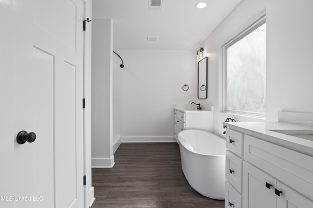 bathroom with two vanities, a sink, wood finished floors, a shower, and a soaking tub