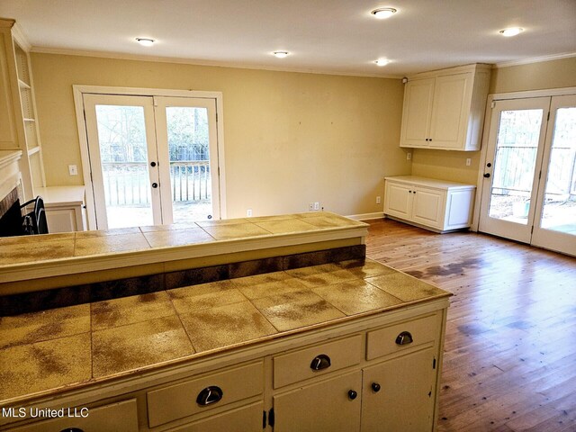 kitchen featuring crown molding, a tile fireplace, tile counters, light hardwood / wood-style floors, and french doors