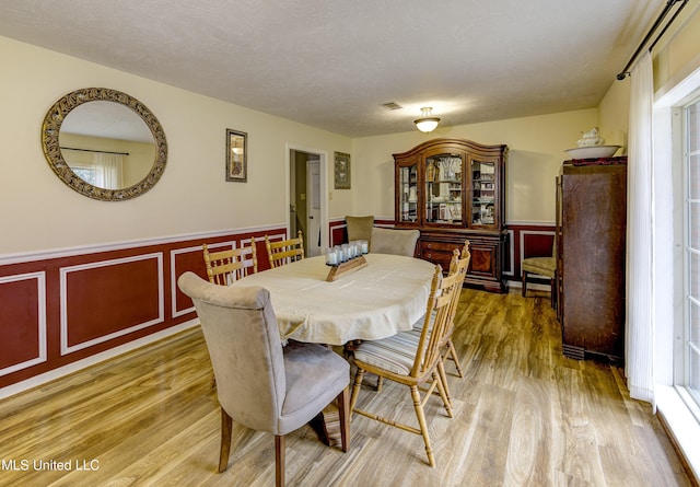 911 Newitt Vick Dr, Vicksburg, MS 39183 - dining space with light wood-style flooring, a wainscoted wall, plenty of natural light, and a decorative wall