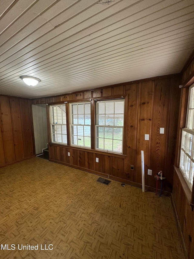 unfurnished room featuring dark parquet flooring, a wealth of natural light, and wooden walls