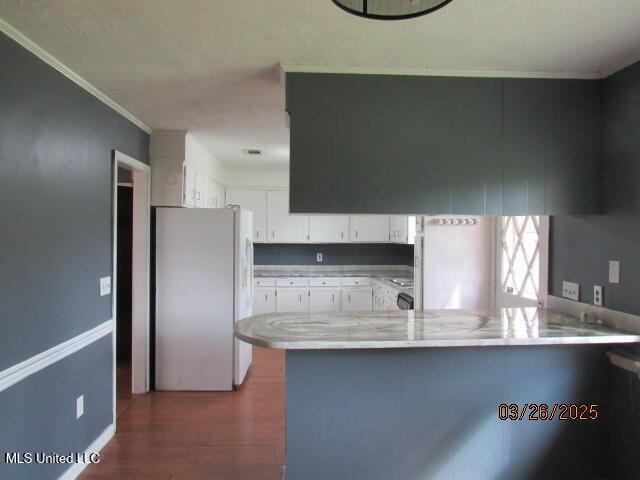 kitchen with wood finished floors, freestanding refrigerator, white cabinets, ornamental molding, and a peninsula