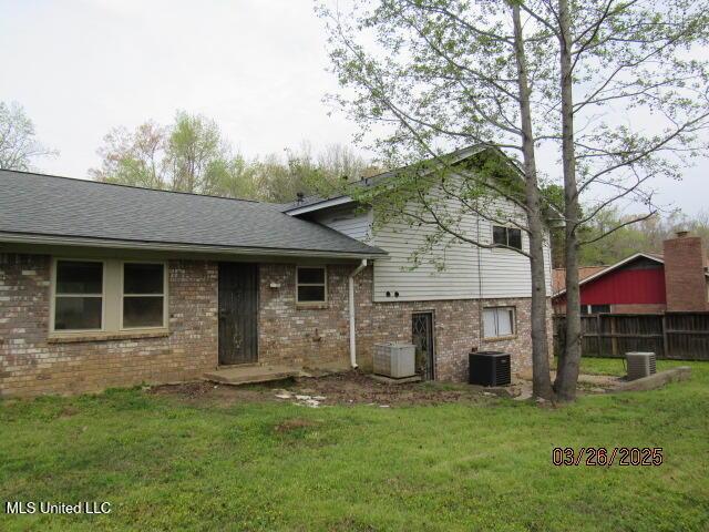 back of property featuring a lawn, fence, central AC unit, and brick siding