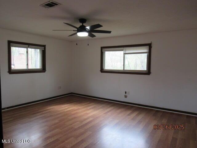 empty room with a ceiling fan, visible vents, wood finished floors, and baseboards