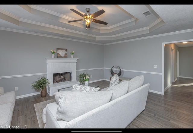 living room featuring a brick fireplace, a tray ceiling, and ornamental molding