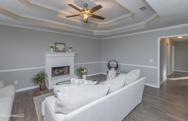 living room featuring a brick fireplace, hardwood / wood-style floors, crown molding, and a raised ceiling