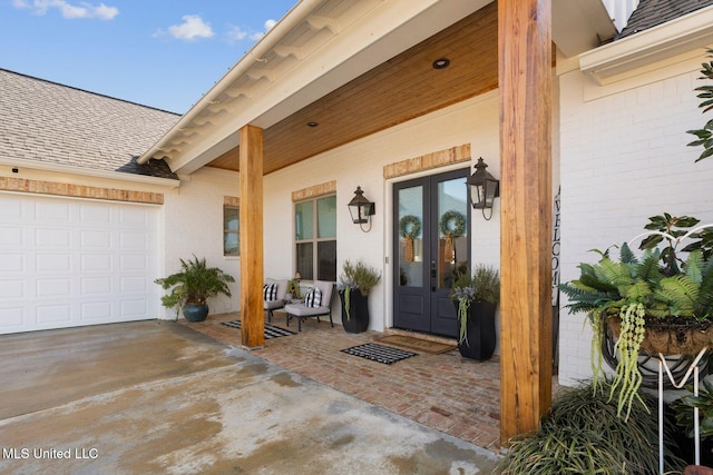 property entrance featuring brick siding, french doors, a garage, and roof with shingles