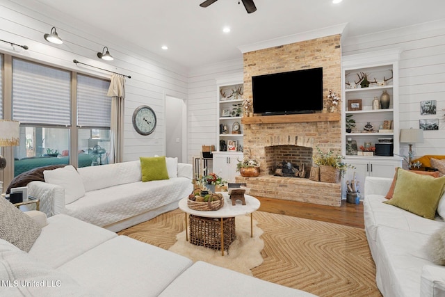 living area featuring built in shelves, wood finished floors, wooden walls, a fireplace, and ceiling fan