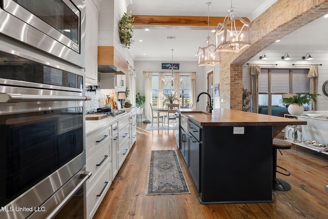 kitchen featuring dark wood-style floors, white cabinets, stainless steel appliances, wood counters, and a kitchen island with sink