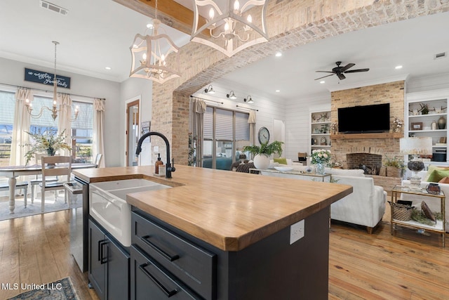 kitchen with visible vents, butcher block countertops, a kitchen island with sink, a sink, and hardwood / wood-style floors