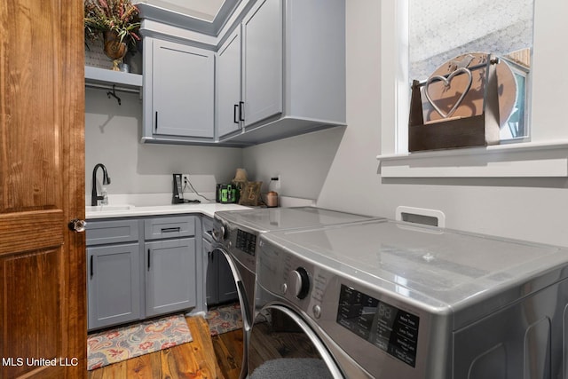 laundry area featuring cabinet space, washer and dryer, wood finished floors, and a sink