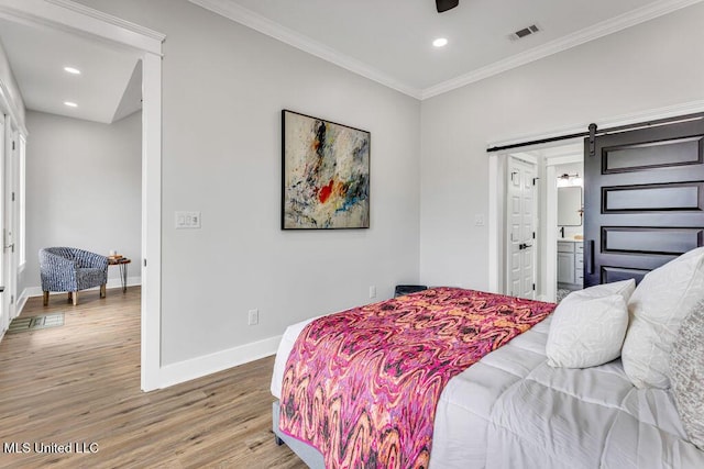 bedroom featuring hardwood / wood-style floors, a barn door, ensuite bath, and crown molding