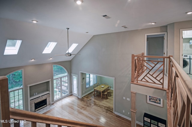 living room featuring washer / clothes dryer, a tiled fireplace, light hardwood / wood-style floors, ceiling fan, and high vaulted ceiling