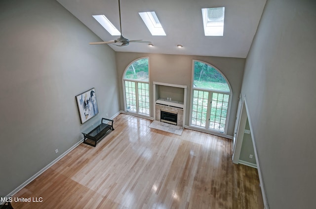 unfurnished living room featuring ceiling fan, high vaulted ceiling, a skylight, and light hardwood / wood-style flooring