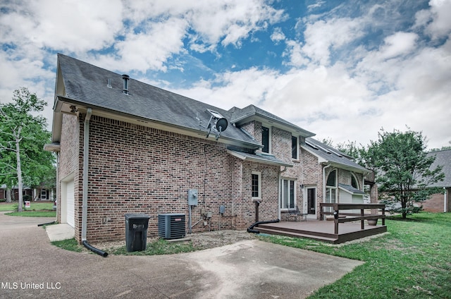 rear view of property featuring a wooden deck, a yard, a garage, and central air condition unit