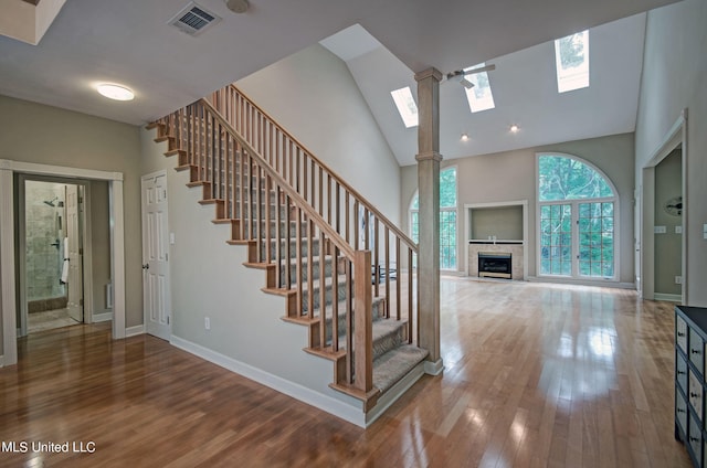 stairway with a tiled fireplace, high vaulted ceiling, a skylight, and hardwood / wood-style floors