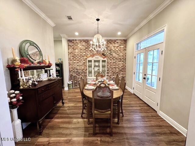 dining room with french doors, dark wood-type flooring, a notable chandelier, ornamental molding, and brick wall