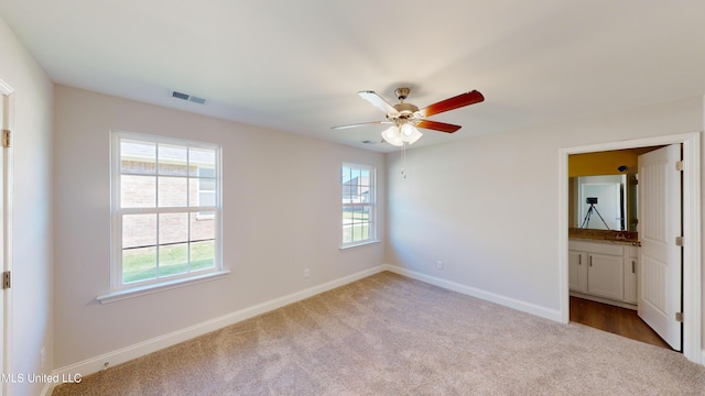 unfurnished bedroom with connected bathroom, multiple windows, ceiling fan, and light colored carpet