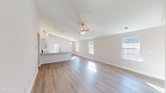 unfurnished living room featuring ceiling fan, sink, wood-type flooring, and vaulted ceiling