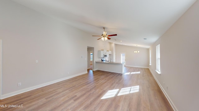 unfurnished living room featuring lofted ceiling, light wood-type flooring, and ceiling fan with notable chandelier