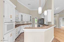 123 Munich Dr, Madison, MS 39110 - kitchen featuring white oven, white cabinets, glass insert cabinets, ornamental molding, and decorative light fixtures
