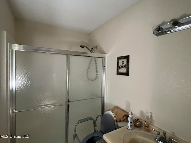 bathroom featuring a shower with shower door and sink