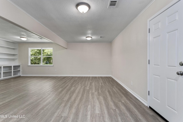 basement featuring wood finished floors, baseboards, a textured ceiling, and visible vents