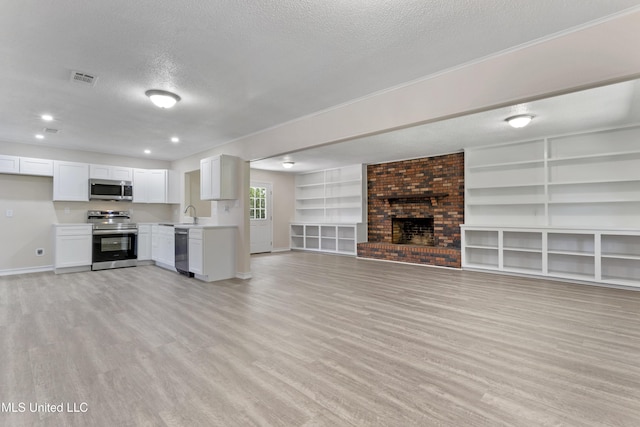 unfurnished living room with a brick fireplace, a textured ceiling, baseboards, and light wood-style floors
