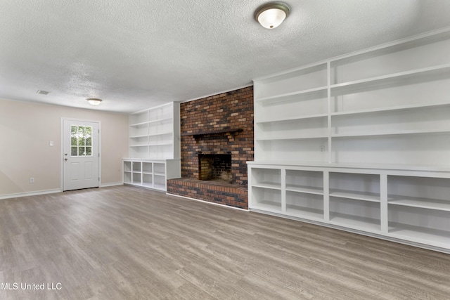 unfurnished living room featuring baseboards, a textured ceiling, a brick fireplace, and wood finished floors