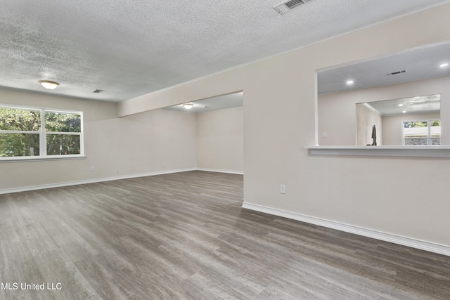 interior space with baseboards, a textured ceiling, wood finished floors, and visible vents
