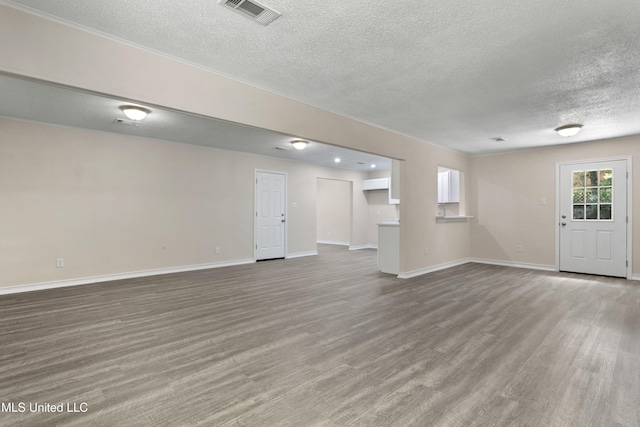 unfurnished living room featuring visible vents, baseboards, a textured ceiling, and wood finished floors