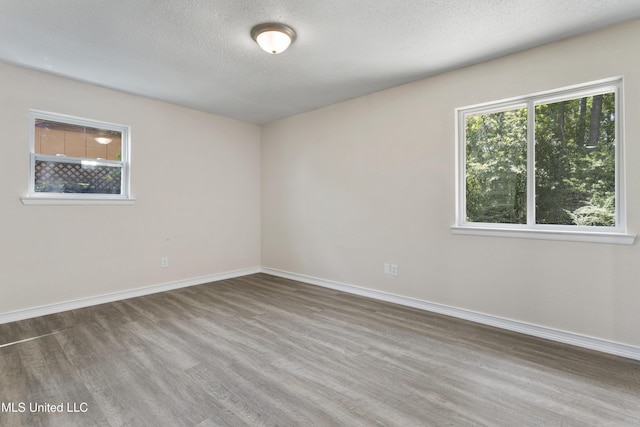 spare room with a textured ceiling, baseboards, and wood finished floors