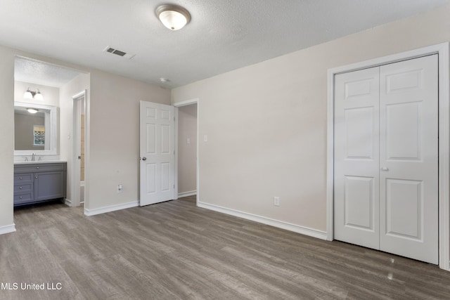 unfurnished bedroom with baseboards, ensuite bath, wood finished floors, and visible vents