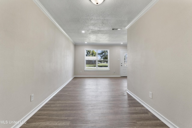 empty room with dark wood-style flooring, a textured ceiling, visible vents, baseboards, and ornamental molding