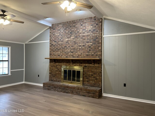 unfurnished living room featuring ceiling fan, a brick fireplace, vaulted ceiling with beams, crown molding, and wood-type flooring