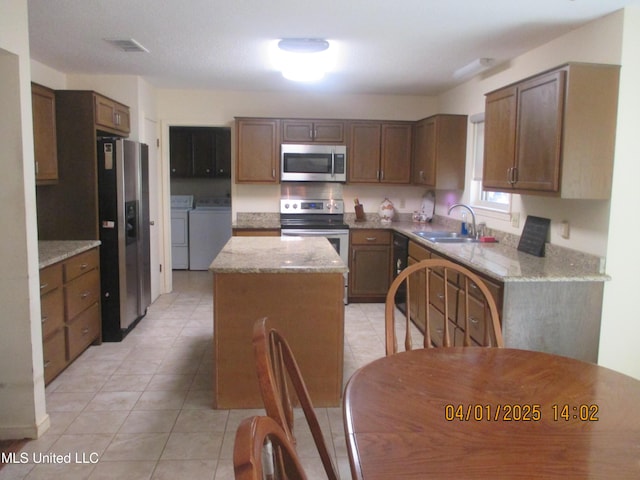 kitchen featuring visible vents, stainless steel appliances, a sink, washer and dryer, and a center island