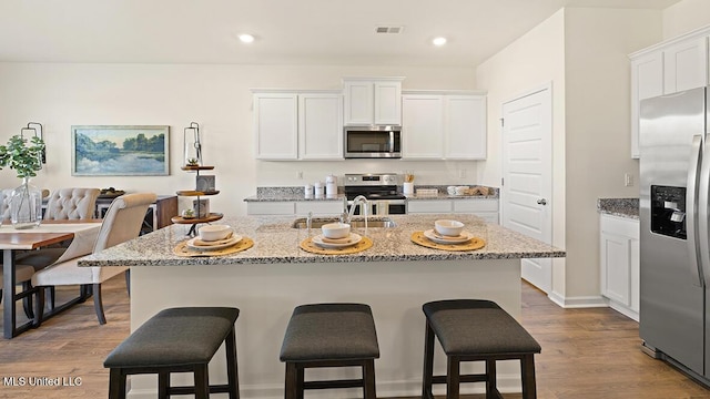 kitchen featuring white cabinets, a kitchen island with sink, appliances with stainless steel finishes, and hardwood / wood-style floors