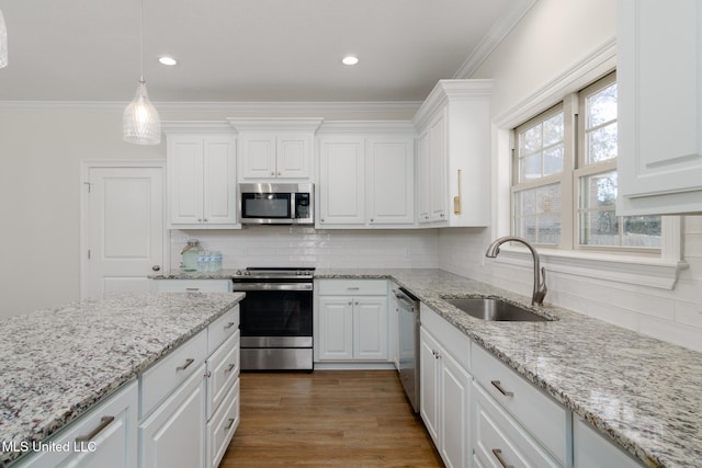 kitchen featuring sink, white cabinetry, hanging light fixtures, stainless steel appliances, and ornamental molding