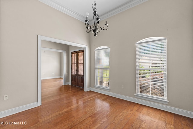 empty room with a chandelier, wood finished floors, crown molding, and baseboards