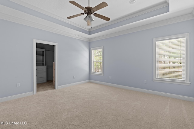 empty room with a tray ceiling, ornamental molding, light carpet, ceiling fan, and baseboards