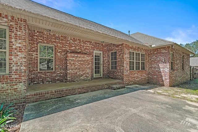 back of house featuring brick siding, a patio, and roof with shingles