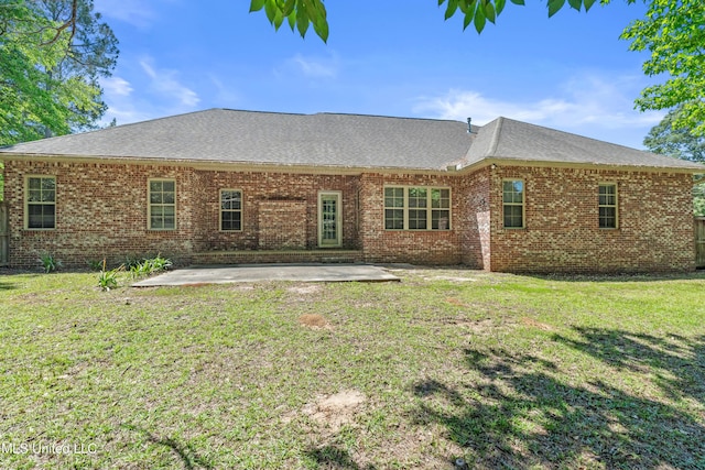 back of house with brick siding, a patio area, a shingled roof, and a yard