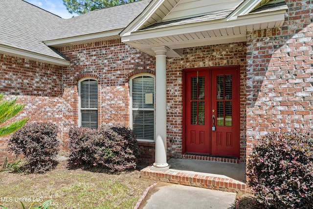 view of exterior entry featuring brick siding, a shingled roof, and french doors