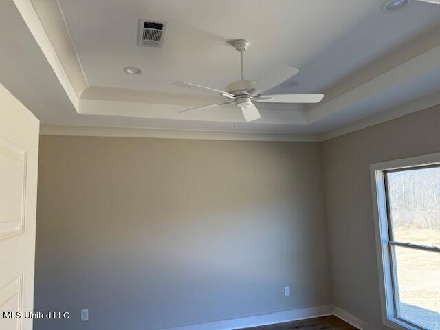 empty room with a raised ceiling, ceiling fan, and ornamental molding