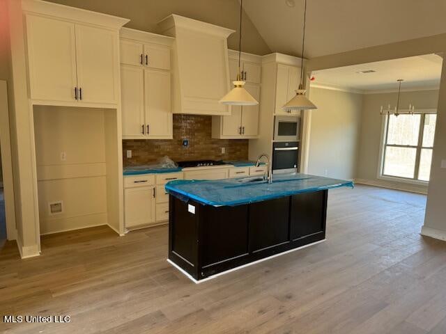 kitchen with white microwave, light hardwood / wood-style flooring, lofted ceiling, and an island with sink